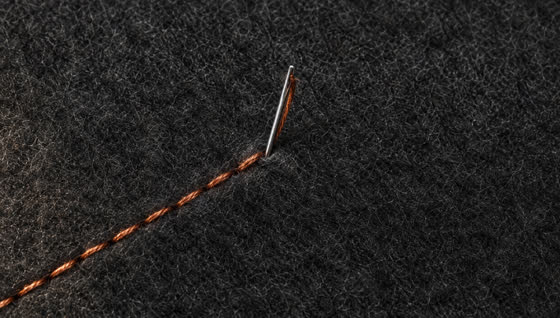 A needle mid-stitch with copper thread on charcoal felt